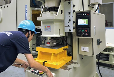 An operator standing at a press control panel with a yellow die set installed in the press