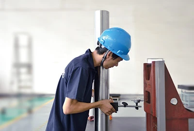 A worker measuring a metal part with a micrometer beside a standing machine structure